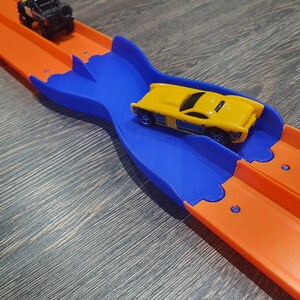 K&ouml;nnte beinhalten: Ein gelbes Spielzeugauto rast auf einer blauen und orangenen Plastikbahn. Die Bahn hat einen gebogenen Abschnitt, der es dem Auto erm&ouml;glicht, die Spur zu wechseln.
