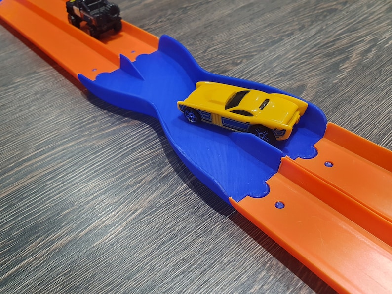 K&ouml;nnte beinhalten: Ein gelbes Spielzeugauto rast auf einer blauen und orangenen Plastikbahn. Die Bahn hat einen gebogenen Abschnitt, der es dem Auto erm&ouml;glicht, die Spur zu wechseln.