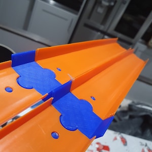 K&ouml;nnte beinhalten: Orangefarbenes und blaues Plastik-Streckenst&uuml;ck f&uuml;r ein Spielzeug-Autorennset. Die Strecke ist so konzipiert, dass sie mit anderen Teilen verbunden werden kann, um eine Rennstrecke zu erstellen.