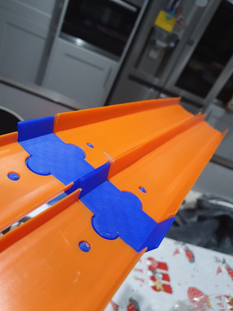 K&ouml;nnte beinhalten: Orangefarbenes und blaues Plastik-Streckenst&uuml;ck f&uuml;r ein Spielzeug-Autorennset. Die Strecke ist so konzipiert, dass sie mit anderen Teilen verbunden werden kann, um eine Rennstrecke zu erstellen.