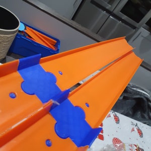 K&ouml;nnte beinhalten: Orangefarbene und blaue Kunststoff-Streckenst&uuml;cke f&uuml;r ein Spielzeug-Autorennset. Die Streckenst&uuml;cke sind so konzipiert, dass sie zusammengef&uuml;gt werden k&ouml;nnen, um eine Rennstrecke zu bilden.