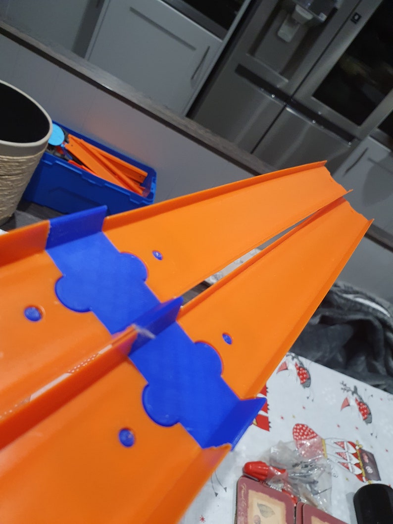 K&ouml;nnte beinhalten: Orangefarbene und blaue Kunststoff-Streckenst&uuml;cke f&uuml;r ein Spielzeug-Autorennset. Die Streckenst&uuml;cke sind so konzipiert, dass sie zusammengef&uuml;gt werden k&ouml;nnen, um eine Rennstrecke zu bilden.