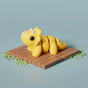 May include: A yellow baby Triceratops dinosaur toy with white horns and black eyes, sitting on a wooden platform with green grass around it.