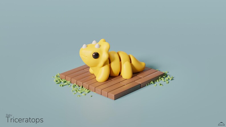 May include: A yellow baby Triceratops dinosaur toy with white horns and black eyes, sitting on a wooden platform with green grass around it.