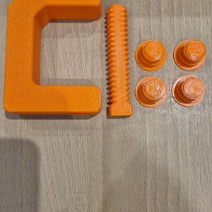 May include: An orange C-clamp with a threaded screw and four orange plastic caps. The clamp is made of plastic and has a textured surface.