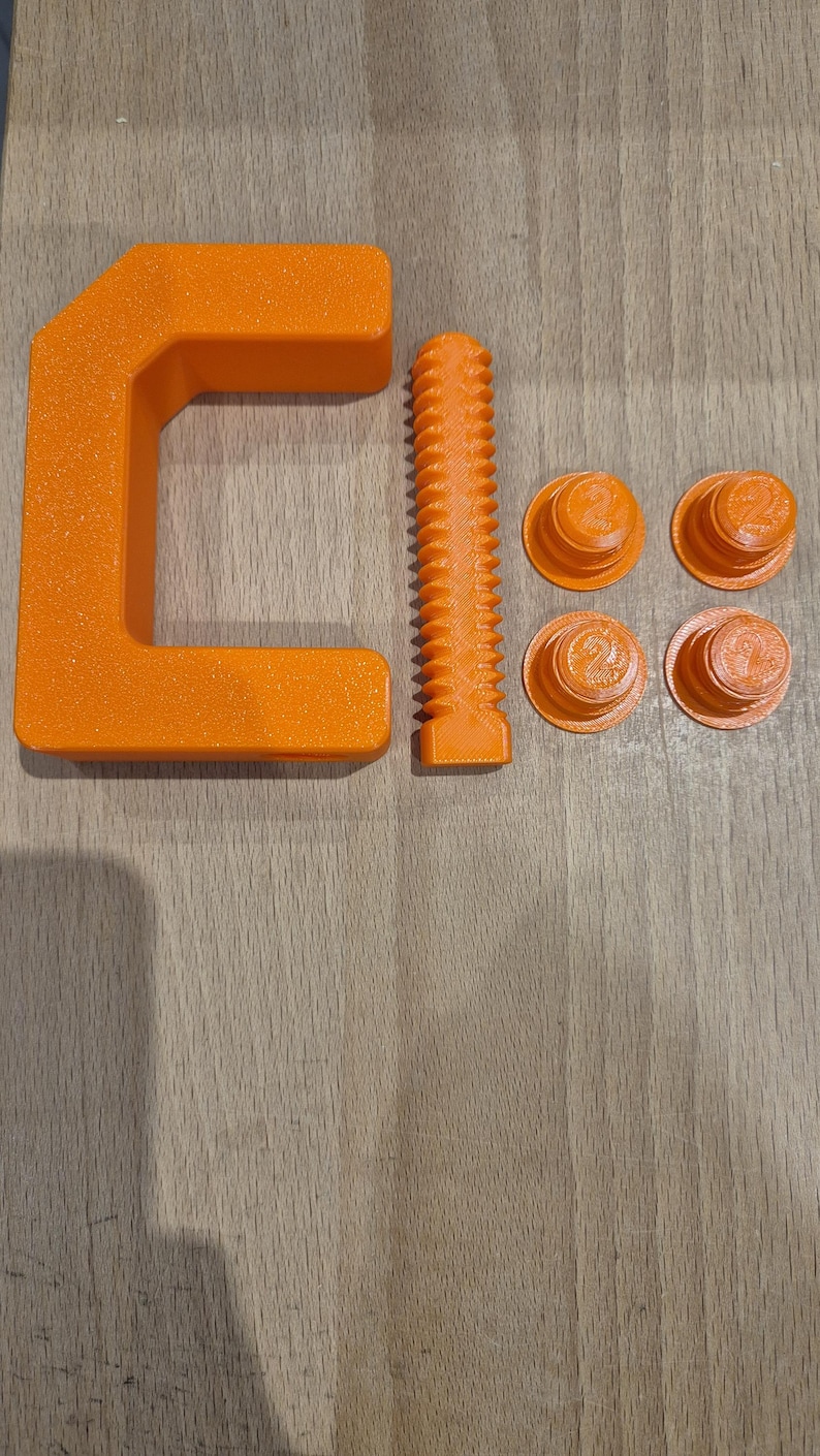 May include: An orange C-clamp with a threaded screw and four orange plastic caps. The clamp is made of plastic and has a textured surface.