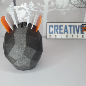 Puede incluir: Un objeto geom&eacute;trico negro impreso en 3D con acentos blancos y naranjas. El objeto tiene una superficie texturizada y est&aacute; dise&ntilde;ado para contener objetos peque&ntilde;os. El objeto est&aacute; etiquetado como "CREATIVE 3D SOLUTIONS".