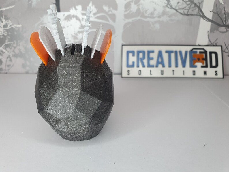 Puede incluir: Un objeto geom&eacute;trico negro impreso en 3D con acentos blancos y naranjas. El objeto tiene una superficie texturizada y est&aacute; dise&ntilde;ado para contener objetos peque&ntilde;os. El objeto est&aacute; etiquetado como "CREATIVE 3D SOLUTIONS".