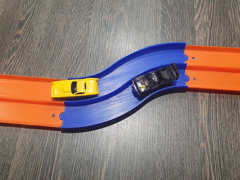 May include: A blue and orange toy race track with two toy cars. One car is yellow and the other is black.