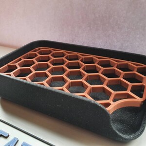 May include: A black soap dish with a honeycomb-shaped insert made of brown plastic. The dish is designed to help soap drain and dry.