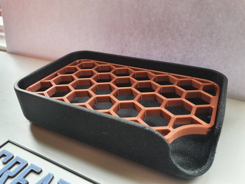 May include: A black soap dish with a honeycomb-shaped insert made of brown plastic. The dish is designed to help soap drain and dry.