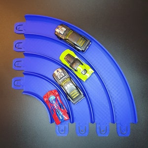 May include: Four toy cars on a blue plastic track. The cars are red, black, green, and gray. The track is curved and has a checkered pattern.