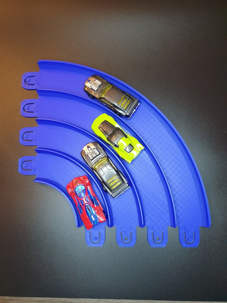 May include: Four toy cars on a blue plastic track. The cars are red, black, green, and gray. The track is curved and has a checkered pattern.