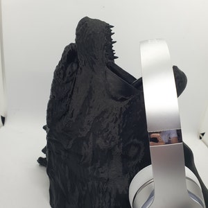 May include: A black 3D printed stand with a textured surface, designed to hold a pair of silver Beats headphones. The headphones have a silver headband and earcups with a red Beats logo.