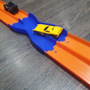 K&ouml;nnte beinhalten: Ein gelbes Spielzeugauto rast auf einer blauen und orangen Plastikbahn. Die Bahn ist so konzipiert, dass Autos die Spur wechseln k&ouml;nnen.