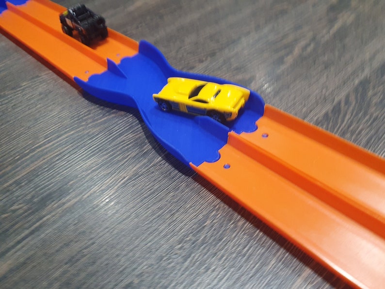 K&ouml;nnte beinhalten: Ein gelbes Spielzeugauto rast auf einer blauen und orangen Plastikbahn. Die Bahn ist so konzipiert, dass Autos die Spur wechseln k&ouml;nnen.