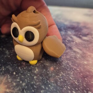 May include: A brown and white 3D printed owl figurine with yellow feet and black eyes. The owl has a small wing on the side.
