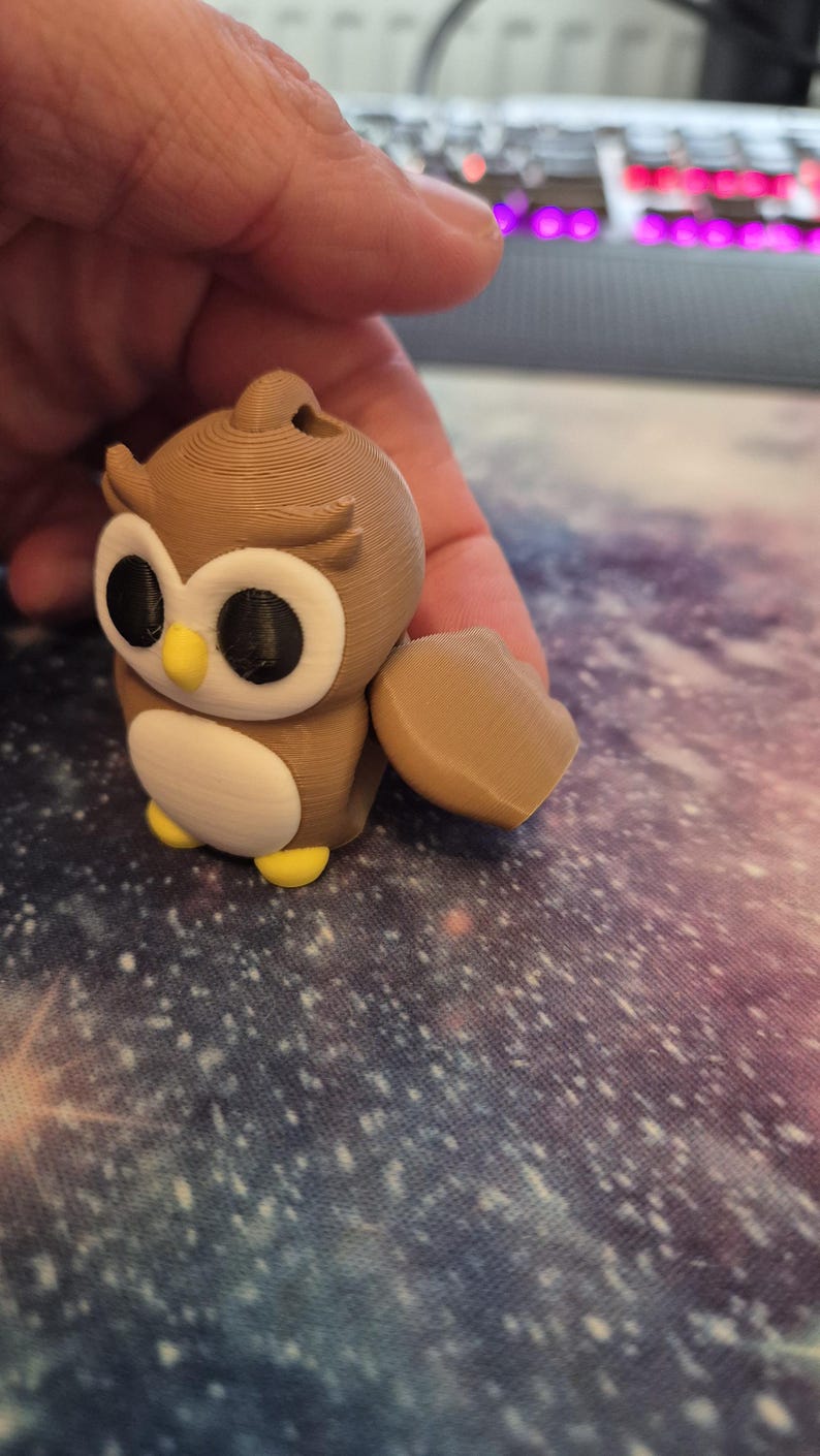 May include: A brown and white 3D printed owl figurine with yellow feet and black eyes. The owl has a small wing on the side.