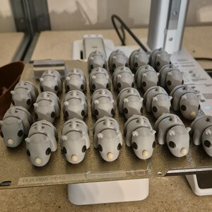 K&ouml;nnte beinhalten: Nahaufnahme einer Gruppe von 3D-gedruckten grauen Nashorn-Figuren auf einer wei&szlig;en Plattform. Die Plattform tr&auml;gt den Text "PLA ABS PLA".