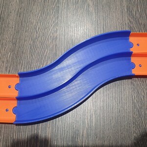 May include: A blue and orange plastic track set for toy cars. The track is curved and has two sections that connect together.