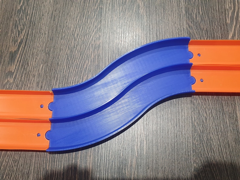 May include: A blue and orange plastic track set for toy cars. The track is curved and has two sections that connect together.