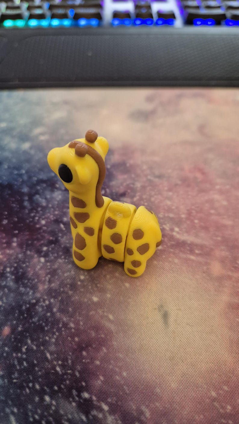 May include: A yellow and brown giraffe figurine with a segmented body. The giraffe has large black eyes and a brown mane.