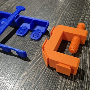 May include: A blue plastic tool with multiple slots and a handle, and an orange plastic clamp with a screw.