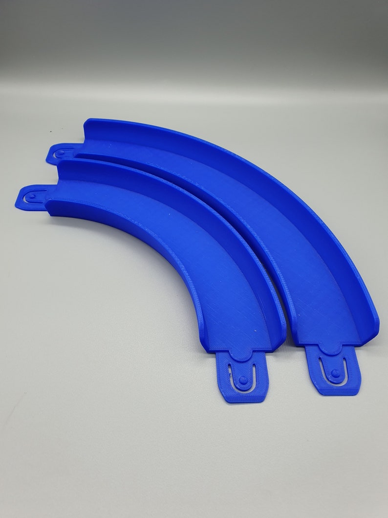 May include: Two blue plastic track pieces for a toy racing car track. The pieces are curved and connect together to form a longer track.