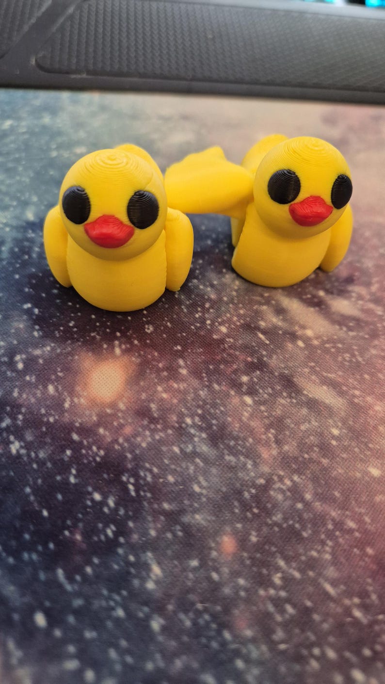 May include: Two yellow rubber duck figurines with black eyes and red beaks. The ducks are facing forward and have a simple design.
