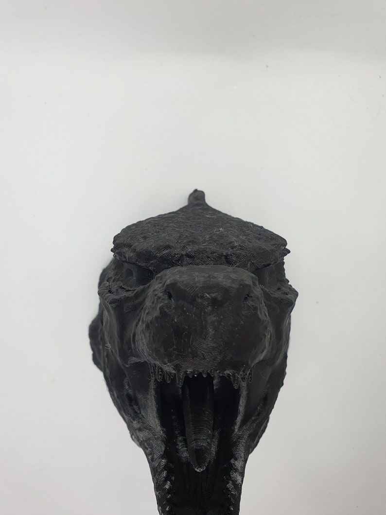 May include: A black 3D printed dinosaur head sculpture with a textured surface and an open mouth.