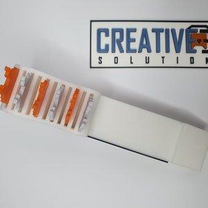 May include: A white plastic storage organizer with slots for holding small objects. The organizer has orange and gray plastic pieces inserted into the slots.