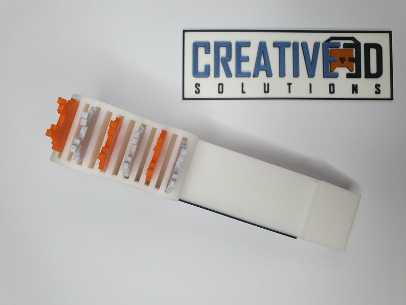 May include: A white plastic storage organizer with slots for holding small objects. The organizer has orange and gray plastic pieces inserted into the slots.