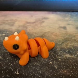 May include: Orange and white segmented toy dinosaur with a large head and small eyes.