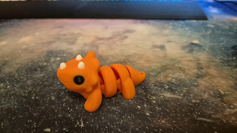 May include: Orange and white segmented toy dinosaur with a large head and small eyes.