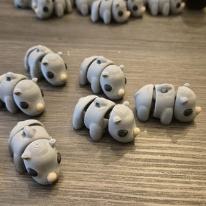 K&ouml;nnte beinhalten: Eine Sammlung von zehn grauen, artikulierten Tierfiguren. Die Figuren sind alle in der gleichen Pose, mit dem Kopf zur Seite geneigt und dem Mund leicht ge&ouml;ffnet. Sie scheinen aus einem glatten, plastischen Material hergestellt zu sein.