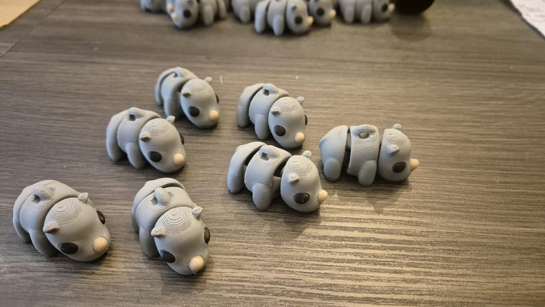 K&ouml;nnte beinhalten: Eine Sammlung von zehn grauen, artikulierten Tierfiguren. Die Figuren sind alle in der gleichen Pose, mit dem Kopf zur Seite geneigt und dem Mund leicht ge&ouml;ffnet. Sie scheinen aus einem glatten, plastischen Material hergestellt zu sein.