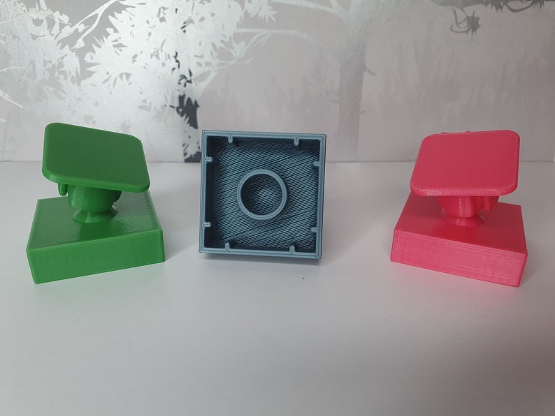 May include: Three 3D printed square blocks, one green, one blue, and one pink. Each block has a small round knob on top.