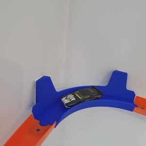 May include: A blue and orange plastic track set for toy cars. The track is curved and mounted on a wall. A black toy car is on the track.