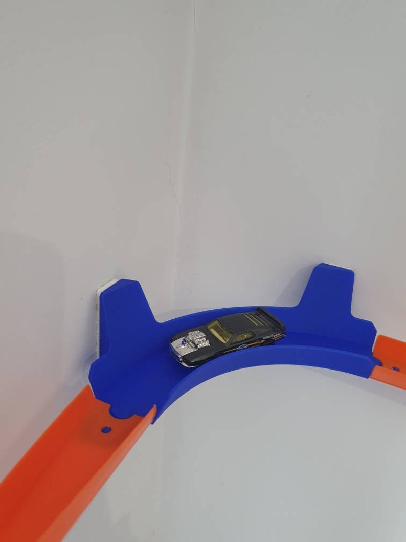 May include: A blue and orange plastic track set for toy cars. The track is curved and mounted on a wall. A black toy car is on the track.
