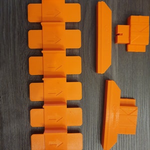 May include: Orange plastic track pieces for a toy car racing set. The track pieces include straight track, a curved track piece, and a track piece with a raised section.