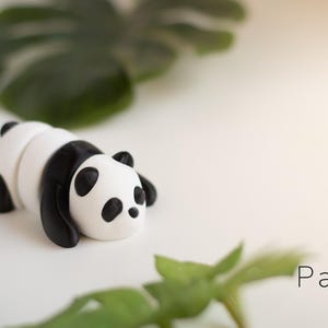 May include: A handcrafted panda figurine in black and white, lying down on a white surface. The panda has black ears, eyes, and limbs. The word "Panda Baby" is written in a minimalist font.
