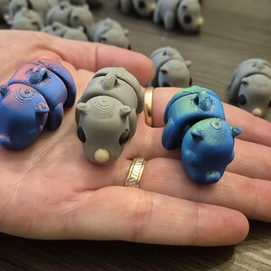 K&ouml;nnte beinhalten: Drei kleine, handbemalte Figuren in Form eines zusammengerollten Tieres. Die Figuren sind in Blaut&ouml;nen und Grau mit einer Metallic-Oberfl&auml;che bemalt.