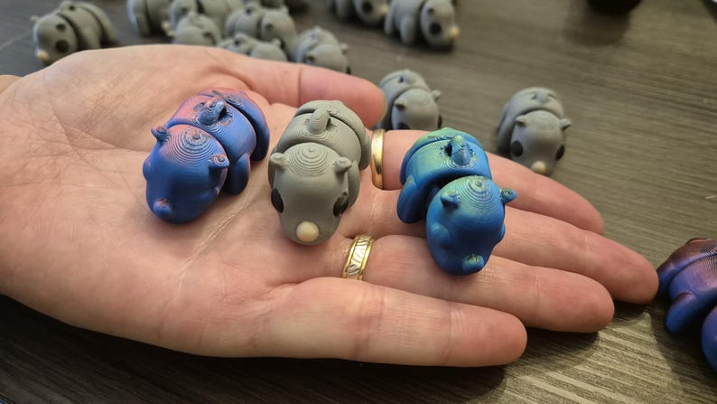 K&ouml;nnte beinhalten: Drei kleine, handbemalte Figuren in Form eines zusammengerollten Tieres. Die Figuren sind in Blaut&ouml;nen und Grau mit einer Metallic-Oberfl&auml;che bemalt.