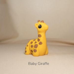 May include: A yellow baby giraffe figurine with brown spots. The giraffe is sitting down with its head up, and has large black eyes. The text "Baby Giraffe" is below the figurine.