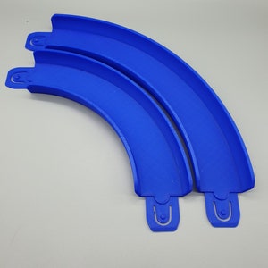 May include: Two blue plastic track pieces for a toy race car track. The pieces are curved and connect together to form a longer track.
