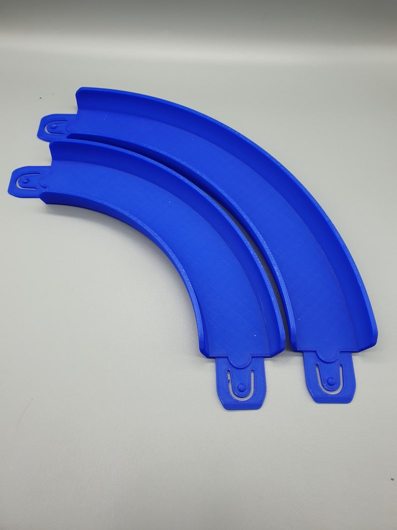 May include: Two blue plastic track pieces for a toy race car track. The pieces are curved and connect together to form a longer track.