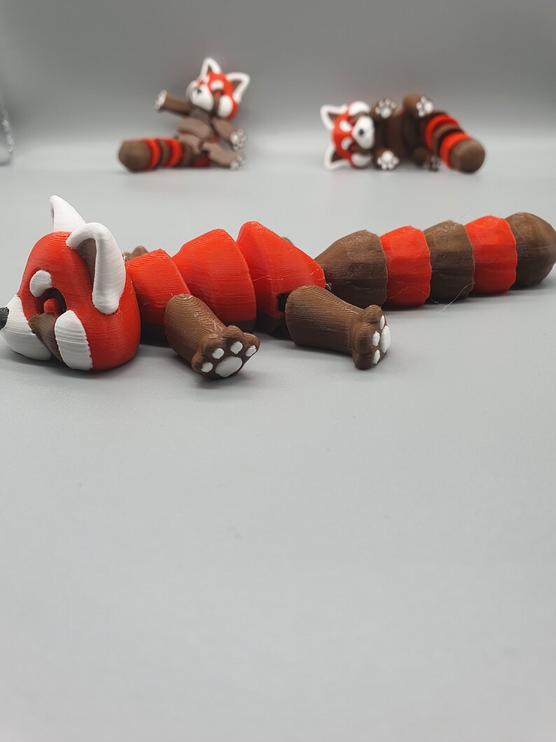 May include: A red panda figurine with segmented body parts, allowing for articulation. The figurine is made of brown and red plastic and has white paw prints on the feet.