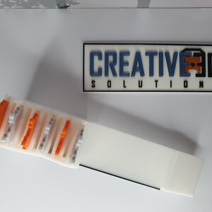May include: A white plastic storage box with a sliding lid. The box is filled with small, colorful plastic blocks. The box is labeled "CREATIVE 3D SOLUTIONS".