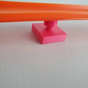 May include: A bright orange plastic track piece with a pink plastic connector piece. The connector piece has a small round knob on top.
