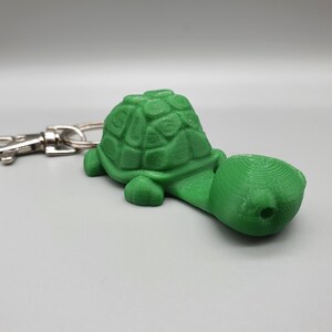 May include: A green plastic turtle keychain with a silver key ring. The turtle has a detailed shell and a long neck.